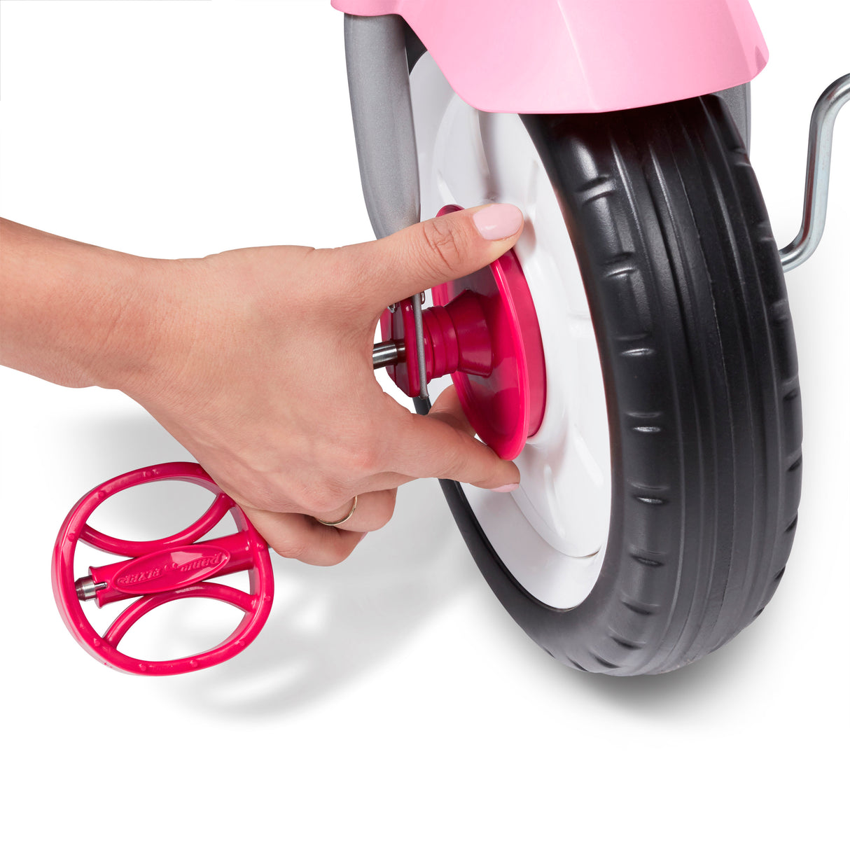 Hand adjusting a pink wheel on a toy tricycle against a white background