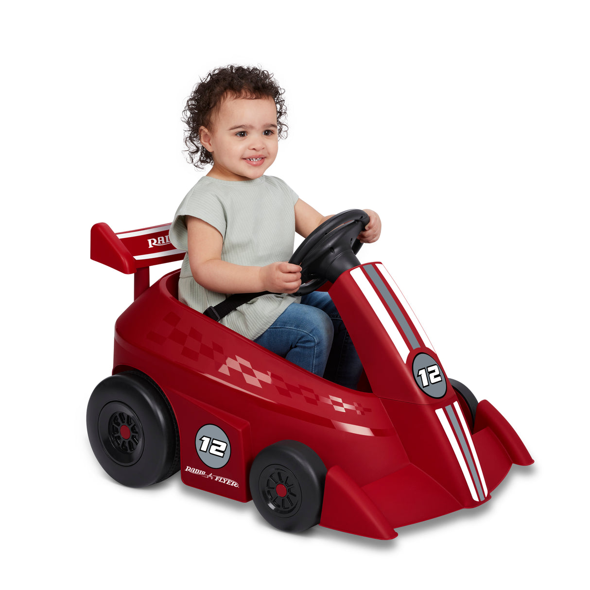 Young child smiling while riding the red Grow With Me Racer with hands on the steering wheel and seat belt fastened