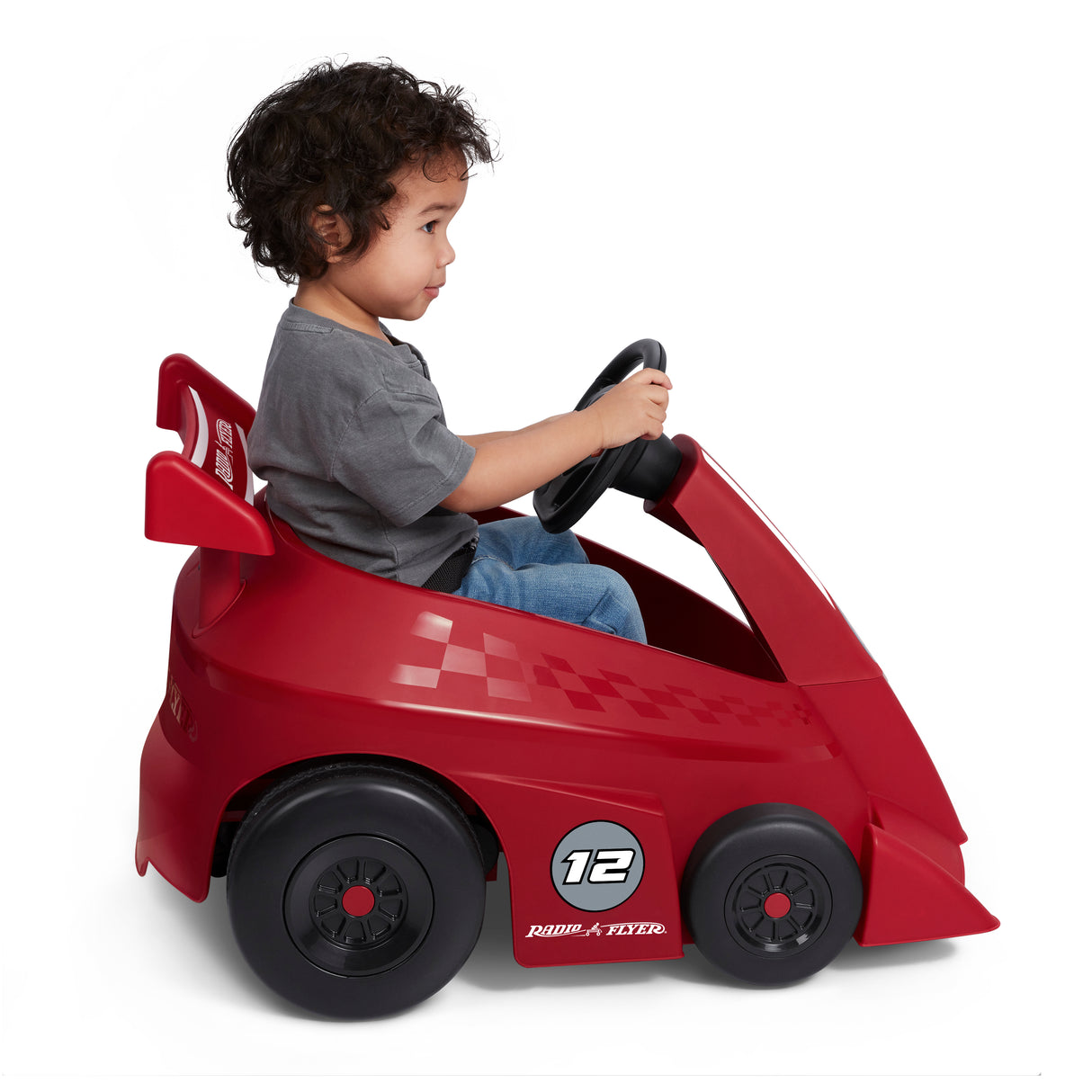 Side profile of a toddler riding the red Grow With Me Racer, showing the racing-inspired design, oversized rear wheels, steering wheel, and seat belt