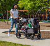Woman Pushing two children riding Voya™ Stroller Wagon through a playground
