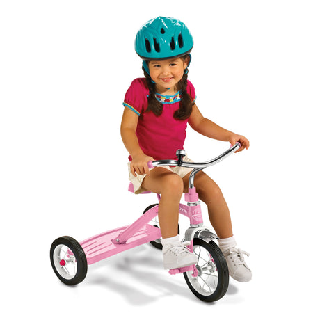 Toddler girl wearing a helmet riding a pink metal classic tricycle on a white background