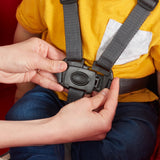 Close-up of a child wearing a yellow shirt and blue jeans seated in a wagon with an adult's hands fastening the 5-point safety harness