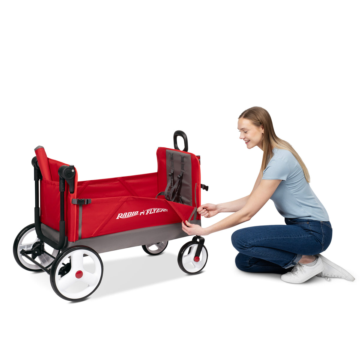 A woman kneels beside a red and gray Radio Flyer wagon, unzipping the side wall. The wagon has white wheels with black tires and a black handle, shown on a clean white background.