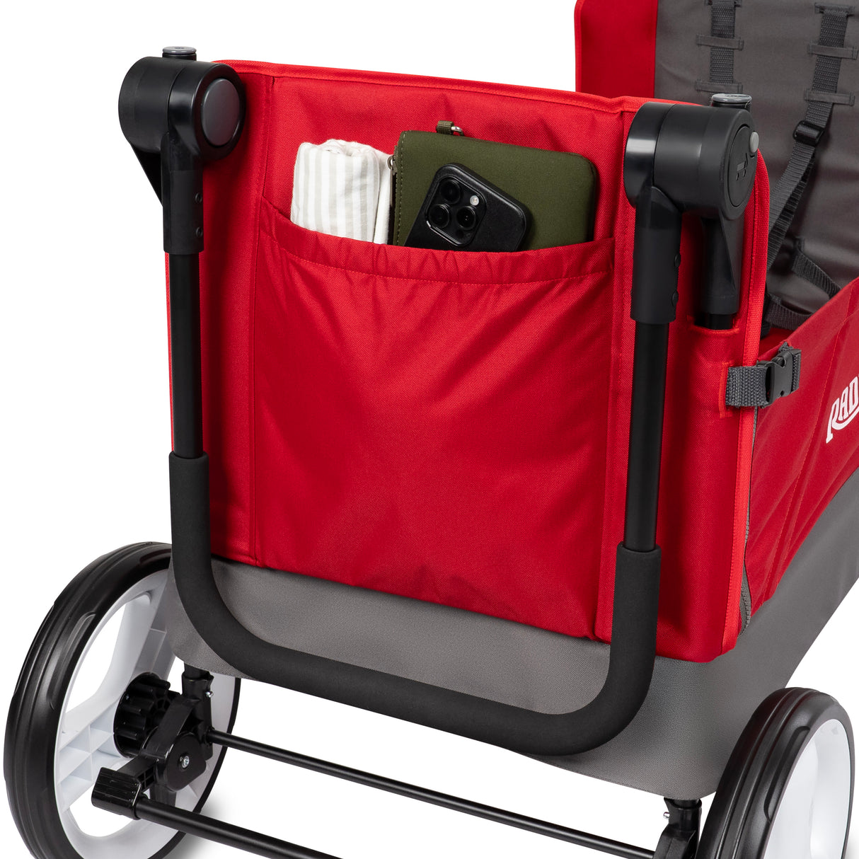 Close-up of the rear storage bag of the red folding wagon. A phone, blanket, and clutch purse are all visible in the storage pouch