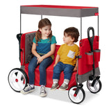 A red Radio Flyer wagon with a canopy, shown with two children sitting inside it in bench mode.