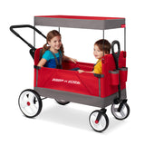 A red and gray Radio Flyer wagon with a canopy, shown with two children sitting inside on a white studio background.