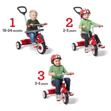 Three children shown riding red tricycles on a white background, each labeled with a number and age range (18-24 months, 2-3 years, 3-5 years). The tricycles have push handles and different handlebar heights, showing progressive stages of use.