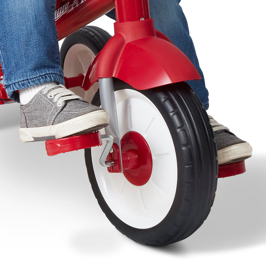 Red tricycle with a child's feet wearing jeans and sneakers on a light gray background