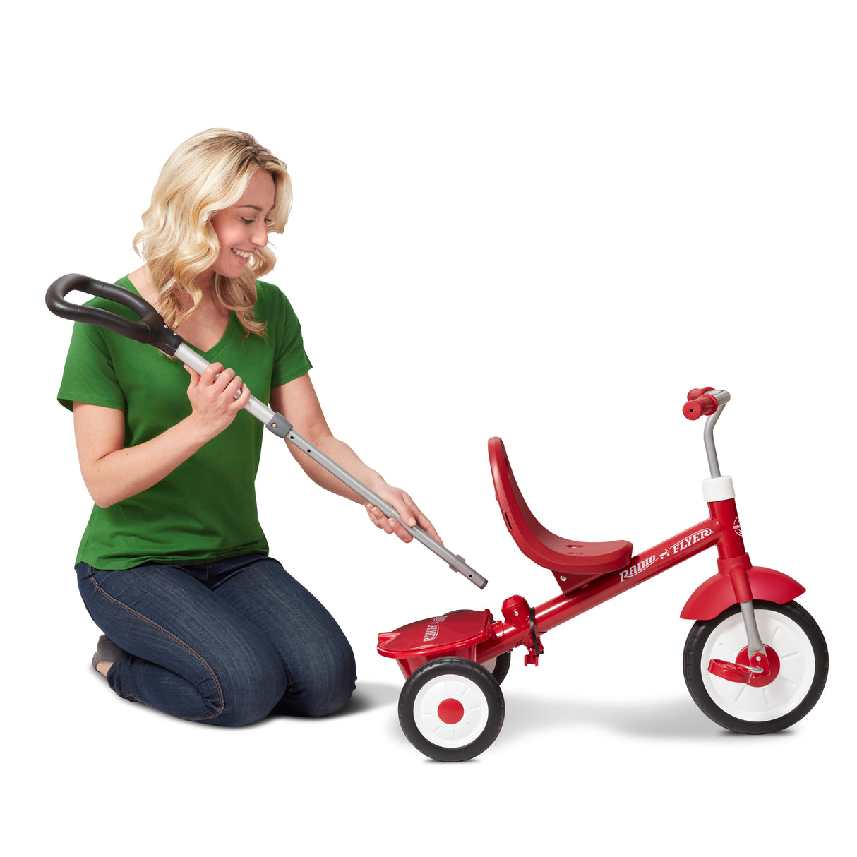 Woman kneeling next to a red tricycle removing the parent push handle on a white background