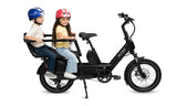 Two children sitting inside the kid hoop accessory on a black electric bike with helmets on a white background