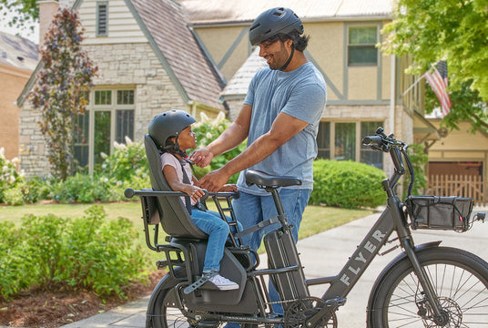 Man and child on a Flyer electric bike with a child seat in a residential area.